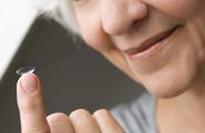 Alte Frau hält eine Kontaktlinse auf dem Finger